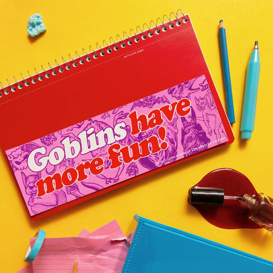 Colorful stationery items including a red notebook with a pink label, pens, and a blue notebook on a yellow background.