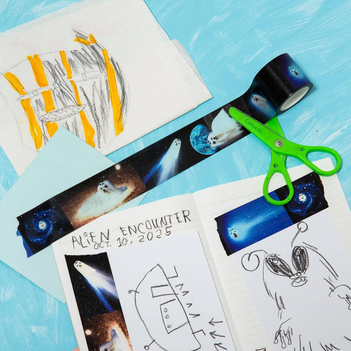 Children's drawings and space-themed ribbon on a blue surface